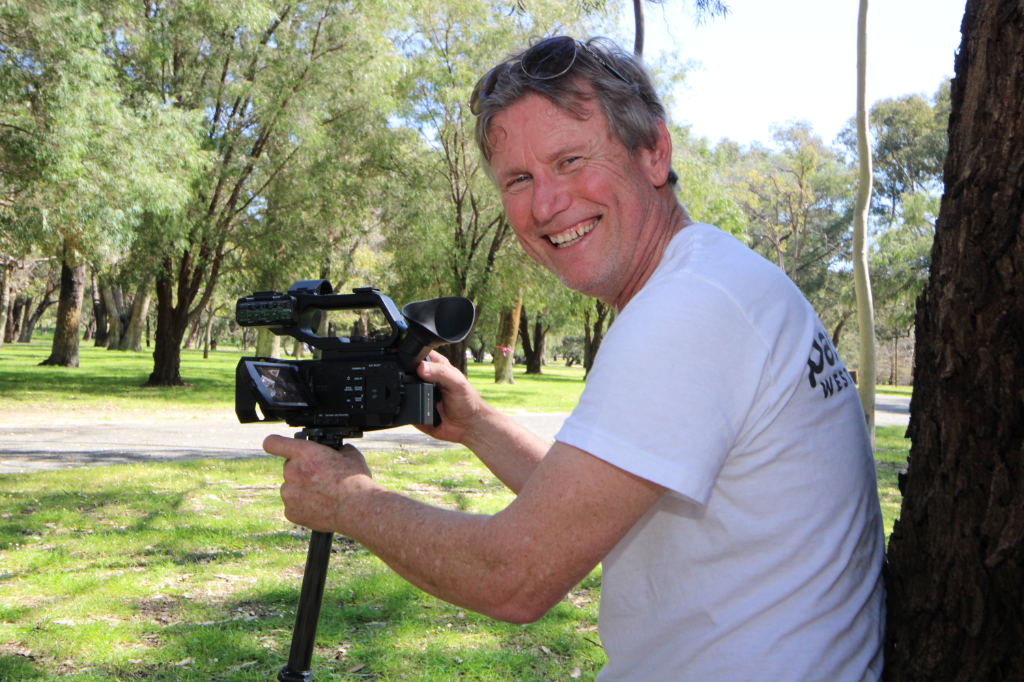 A man holds a camera and smiles over his shoulder.