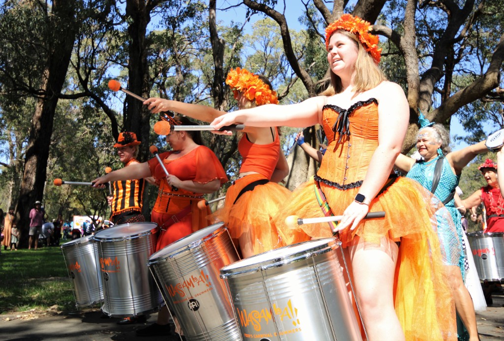 A colourful group of drummers perform for a crowd.